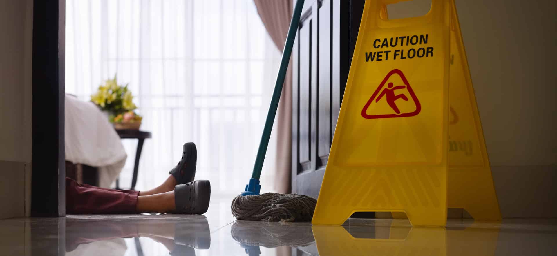 An image of a hotel worker who slipped and fell on slippery floor near a "Caution Wet Floor" sign.