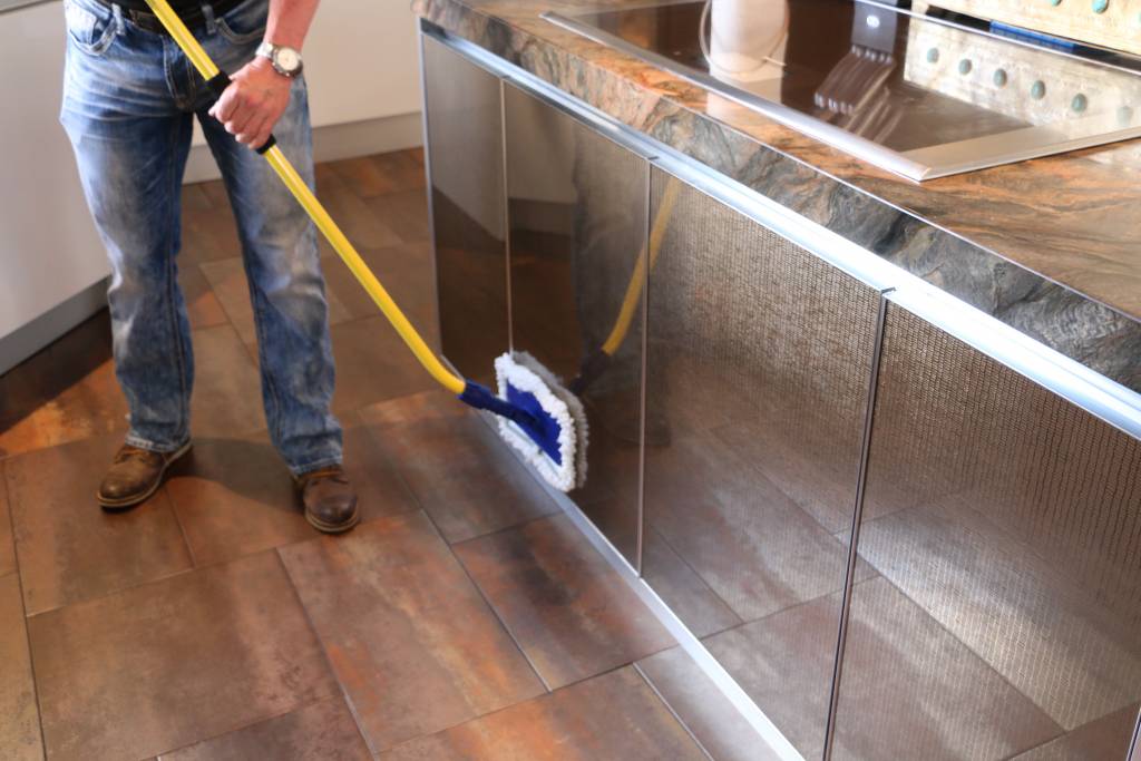 A person uses The Simple Scrub Original cleaning wand to wipe down stainless steel cabinetry in a modern kitchen