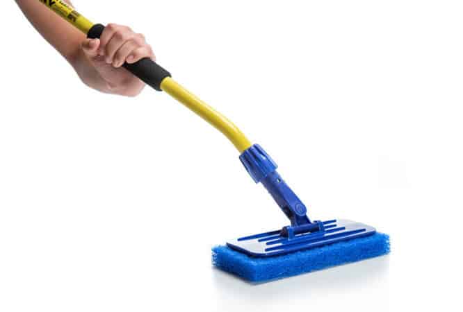 A person holds The Simple Scrub long handled brush equipped with a heavy duty blue pad.